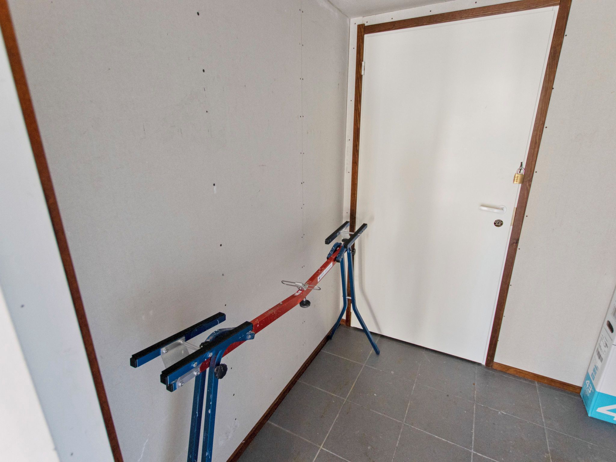 Une pièce avec une porte, un étagère fixée au mur et un sol carrelé.