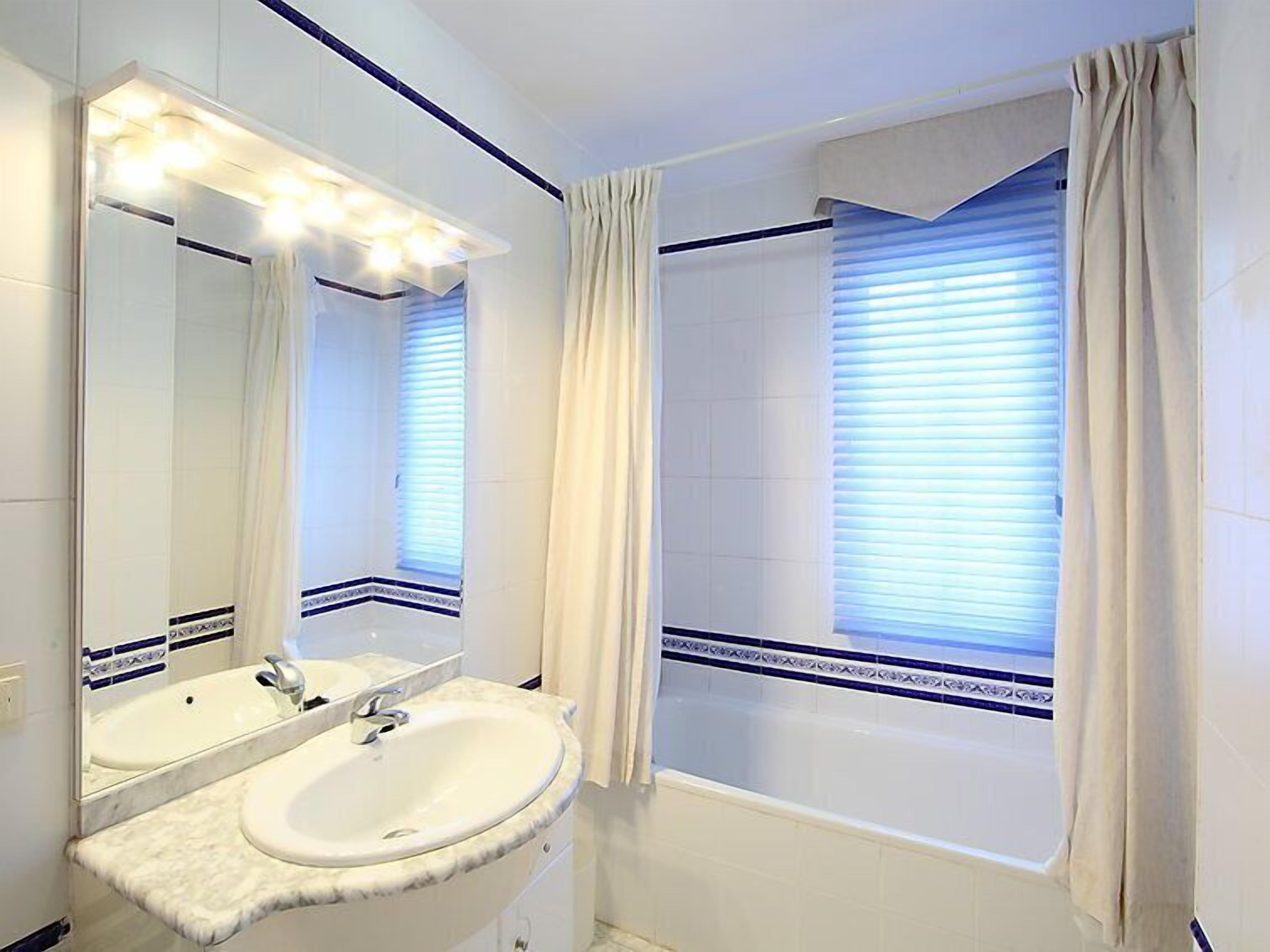 A bathroom with a white sink, mirror, and bathtub.