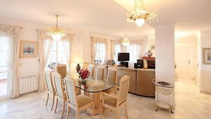 Un ampio soggiorno con un tavolo da pranzo in vetro, comodi posti a sedere, una televisione e un camino.