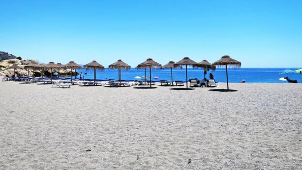 Una spiaggia con ombrelloni di paglia e lettini.