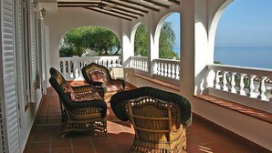 Zona relax esterna riparata, con sedie in vimini e vista sul mare.