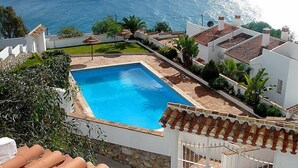 Una piscina con vista sul mare, immersa nel verde e circondata da edifici bianchi con tetti in terracotta.