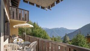 A balcony with a table and chairs, a white umbrella, and a view of mountains. - Apartment Mélèze by Interhome (Ovronnaz)
