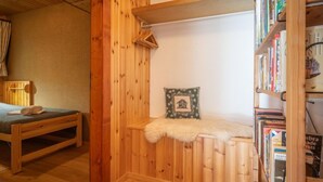 A cozy room with a wooden bed, a small bench, a bookshelf, and a decorative pillow. - Apartment Mélèze by Interhome (Ovronnaz)