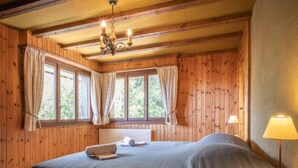 A wooden cabin bedroom with a bed, a chandelier, and a window with curtains. - Apartment Mélèze by Interhome (Ovronnaz)