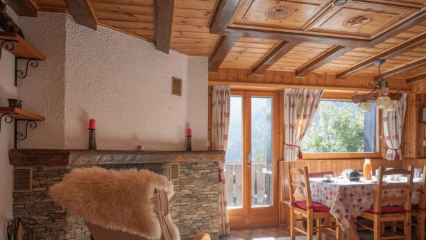 A cozy room with a stone fireplace, wooden ceiling beams, and a dining area with a table and chairs. - Apartment Mélèze by Interhome (Ovronnaz)