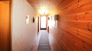 Un couloir en bois, avec une porte sur la gauche, une fenêtre au fond et un luminaire au plafond.