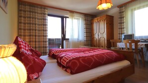 Une chambre à coucher avec un lit, un bureau et une chaise. Il y a une fenêtre avec des rideaux, une porte et une lampe.