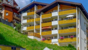 Un hotel de varios pisos con balcones, una colina cubierta de césped y cielo despejado.