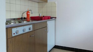 Una cocina con armarios de madera, un refrigerador blanco, un lavamanos con grifo y un recipiente rojo en la encimera.