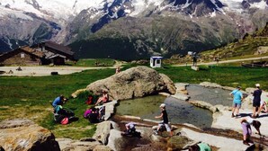 Eine Berglandschaft mit einer kleinen Lodge, einem felsigen Gebiet mit Menschen und einem klaren Himmel.