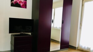 Ein Zimmer mit Fernseher auf einem Schrank, einem Kleiderschrank mit Spiegeln und Holzboden.