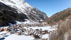 Ein verschneites Dorf mit traditionellen Häusern, einem Berg im Hintergrund und klarem Himmel.