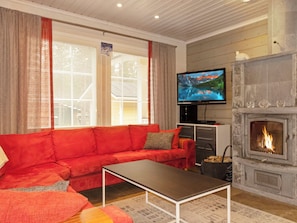 Una sala de estar con un sofá rojo, un televisor de pantalla plana, una chimenea y una ventana con persianas.