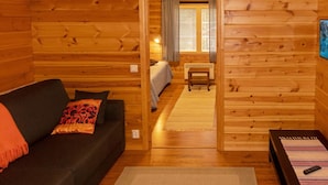 A cozy cabin with a wooden interior, a bed, a small table, and a couch with a throw blanket.