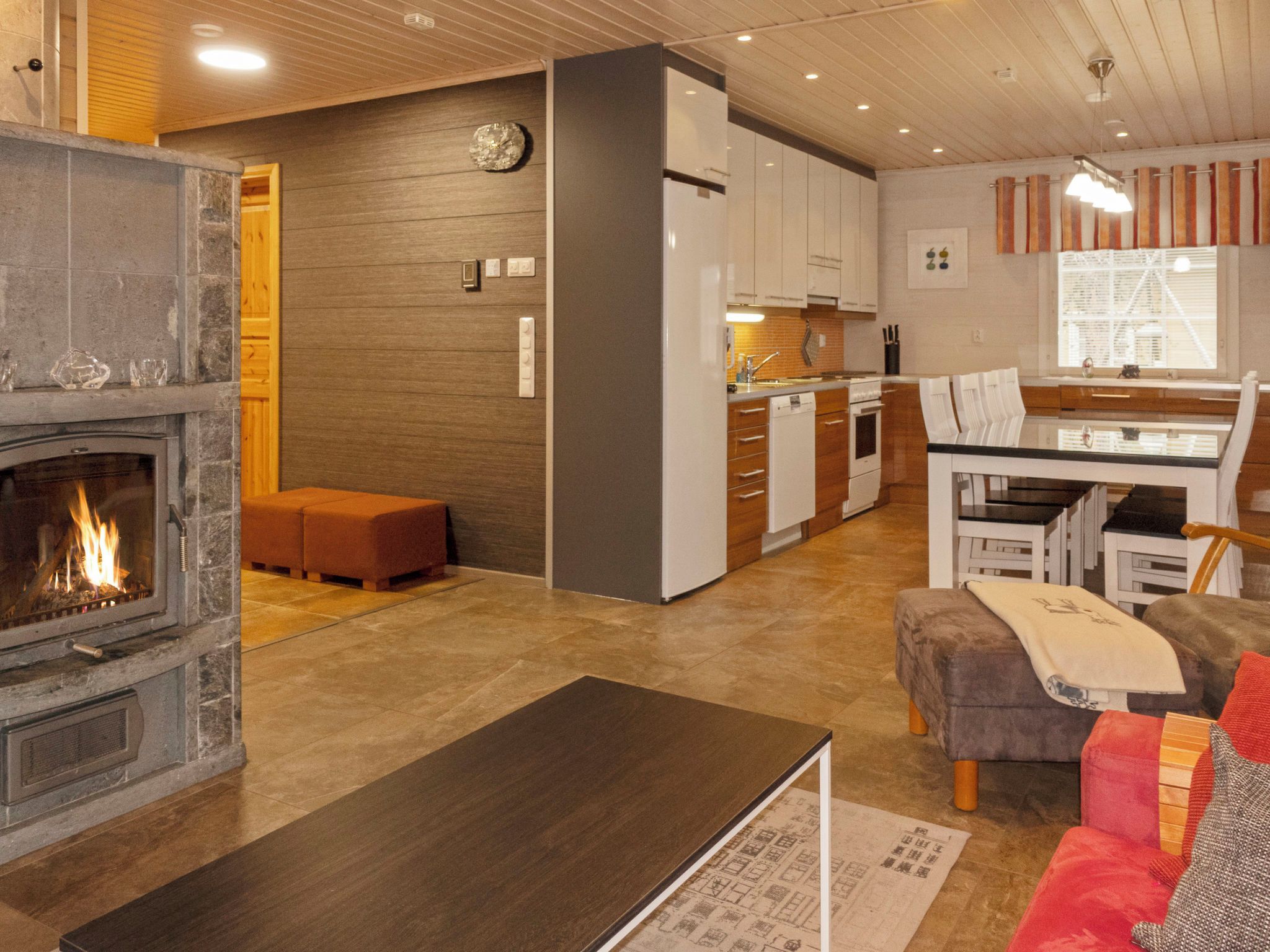 A modern living room with a fireplace, a dining area with a table and chairs, and a kitchen in the background.