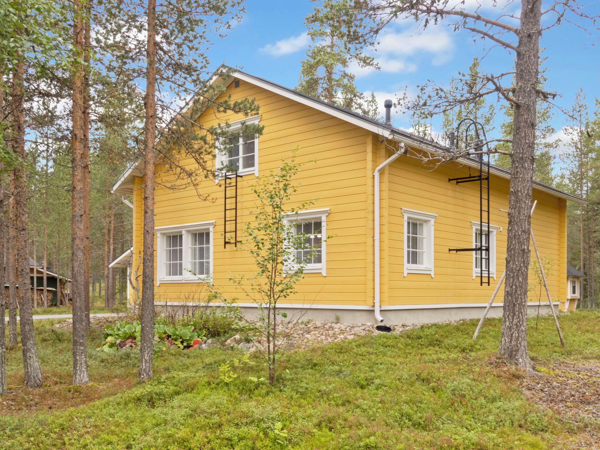 Ett gult hus med ett sadeltak, omgivet av träd och en gräsyta.