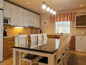 A modern kitchen with white cabinets, a black countertop, and a dining area with white chairs. - Jutapirtti by Interhome (Kittilä)