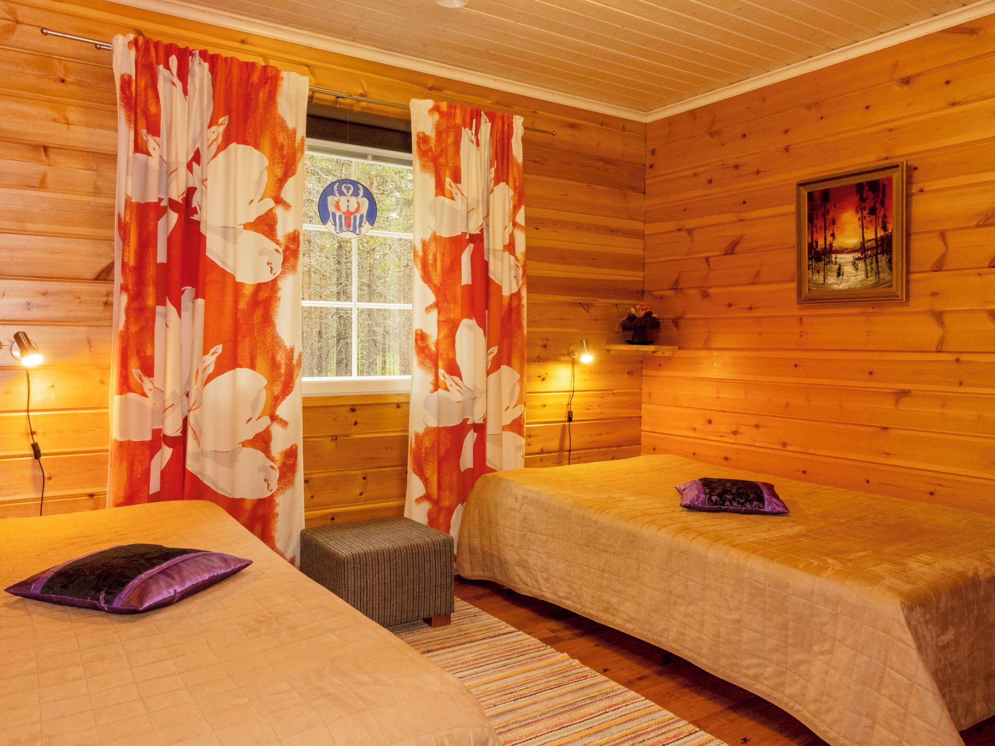 A room with two beds, a window with curtains, a small stool, a painting on the wall, and a lamp on a bedside table.