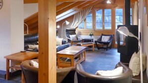 Ein gemütliches Wohnzimmer im Loft-Stil mit hohen Decken, Holzbalken und großen Fenstern. Es gibt Ledersofas, einen Holztisch und eine Stehlampe.