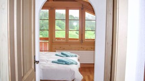 Ein Schlafzimmer mit einem hölzernen Bett, weißer Bettwäsche und Blick auf eine grüne Landschaft durch große Fenster.