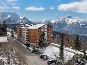 Ein mehrstöckiges Hotel mit Balkonen, ein Skigebiet im Hintergrund und verschneite Umgebung.