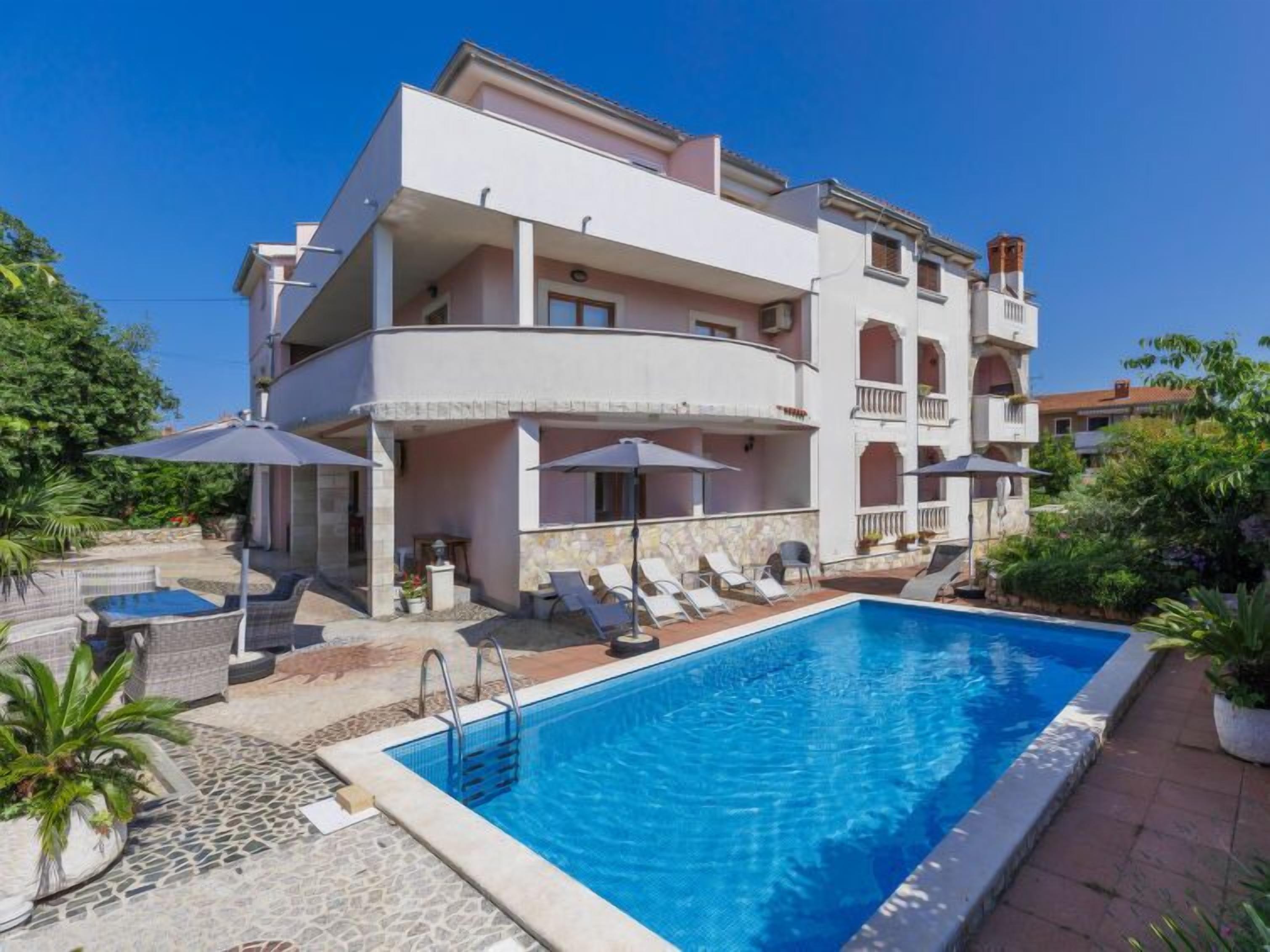 A multi-story hotel with a swimming pool, outdoor seating, and a stone-tiled patio.