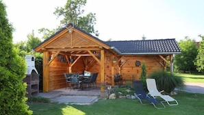 En træhytte med en overdækket terrasse, grill og udendørs møbler.