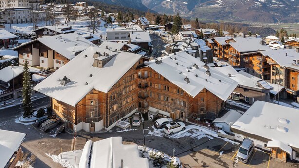 Un paese innevato con edifici tradizionali in legno, una piazza centrale e montagne sullo sfondo.