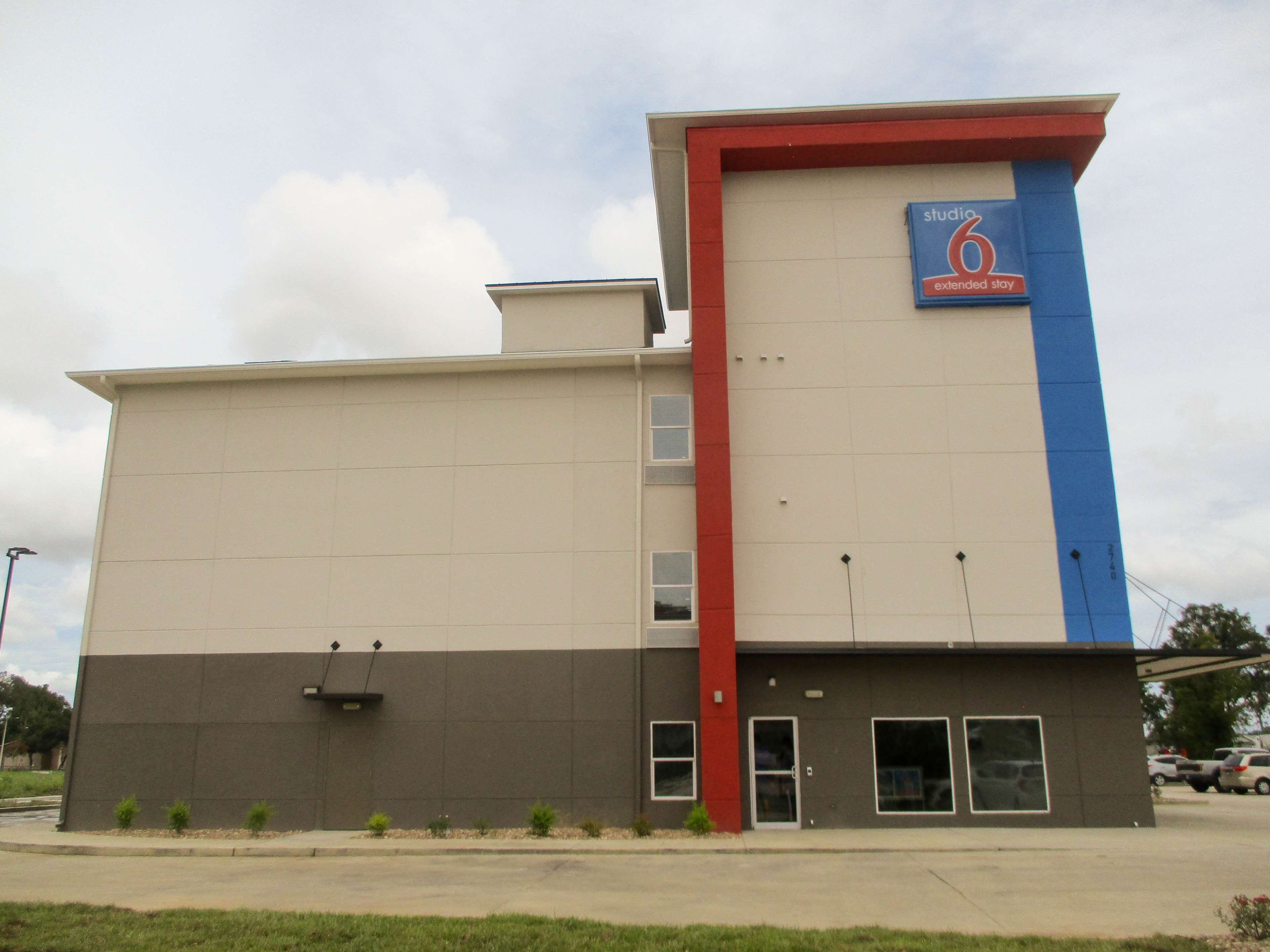 A hotel with a flat facade, a prominent blue and red vertical stripe, and a sign indicating it is a 'studio 6 extended stay' hotel.