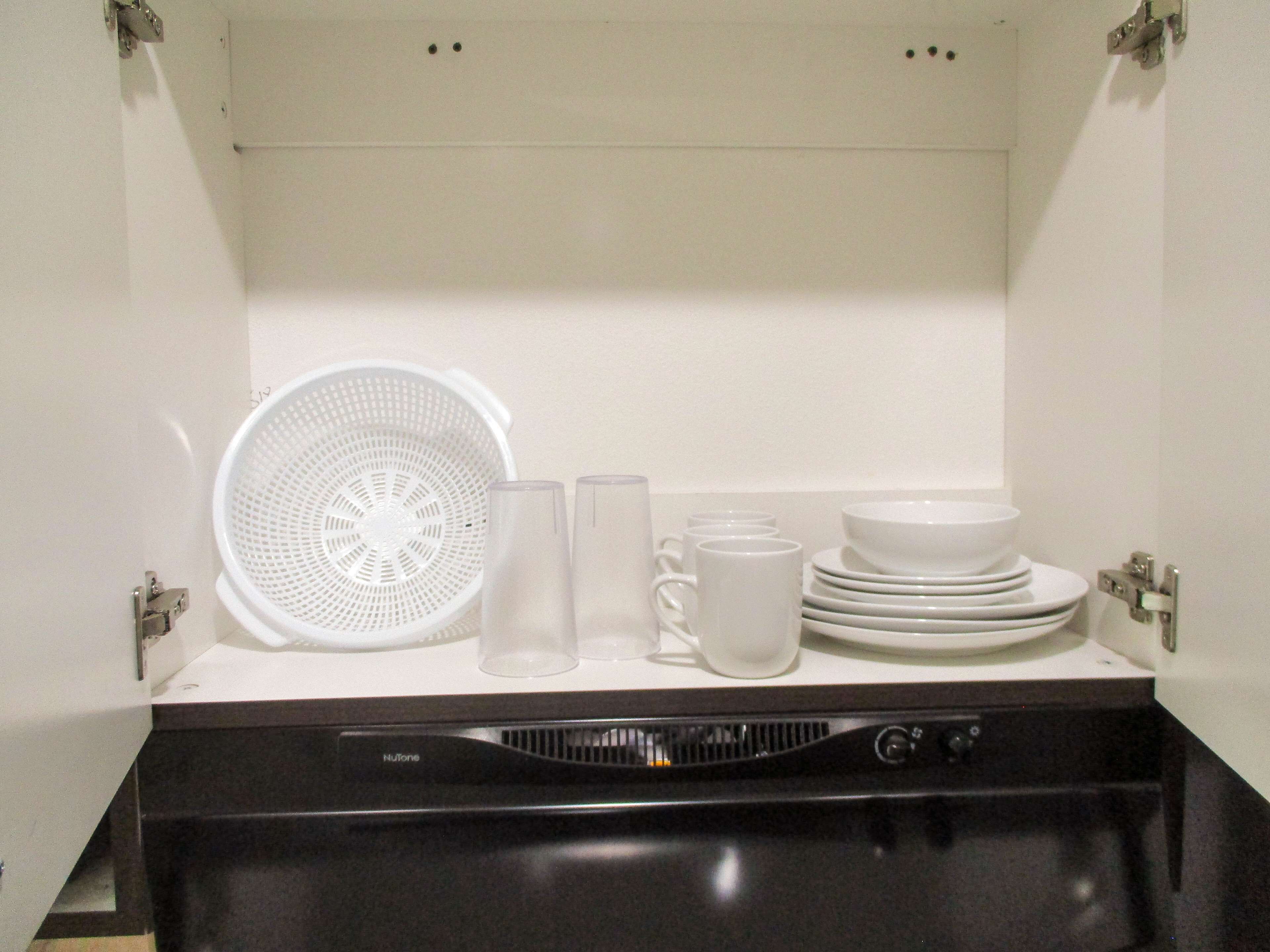 A kitchen area with a dishwasher, a colander, and various white dishes and cups.