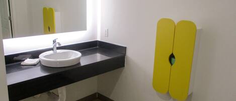 A bathroom with a white sink, a mirror, and a toilet. There are yellow hand dryers on the wall.