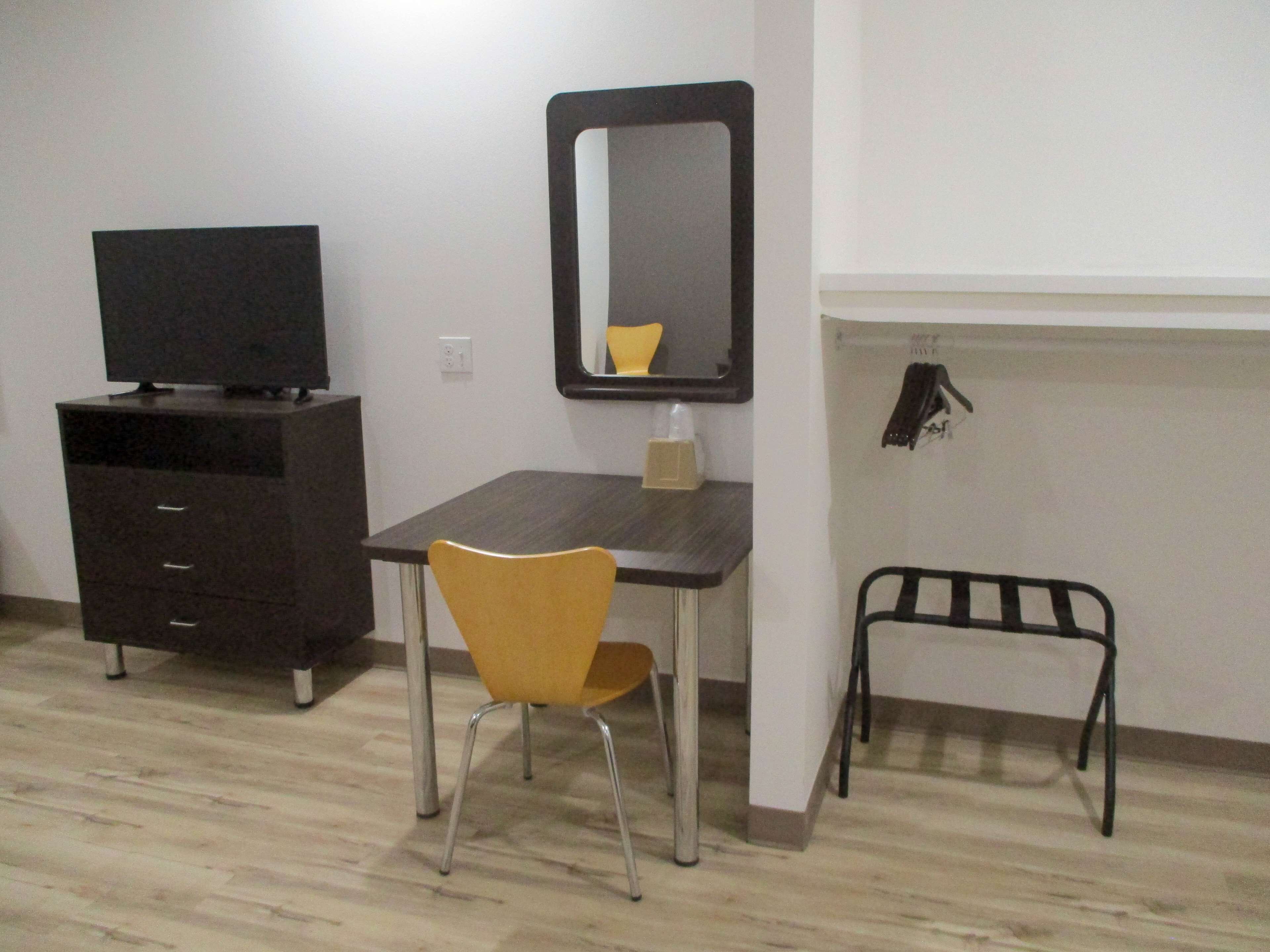 A small, functional room with a desk, a chair, a television on a cabinet, a mirror, and a coat rack.