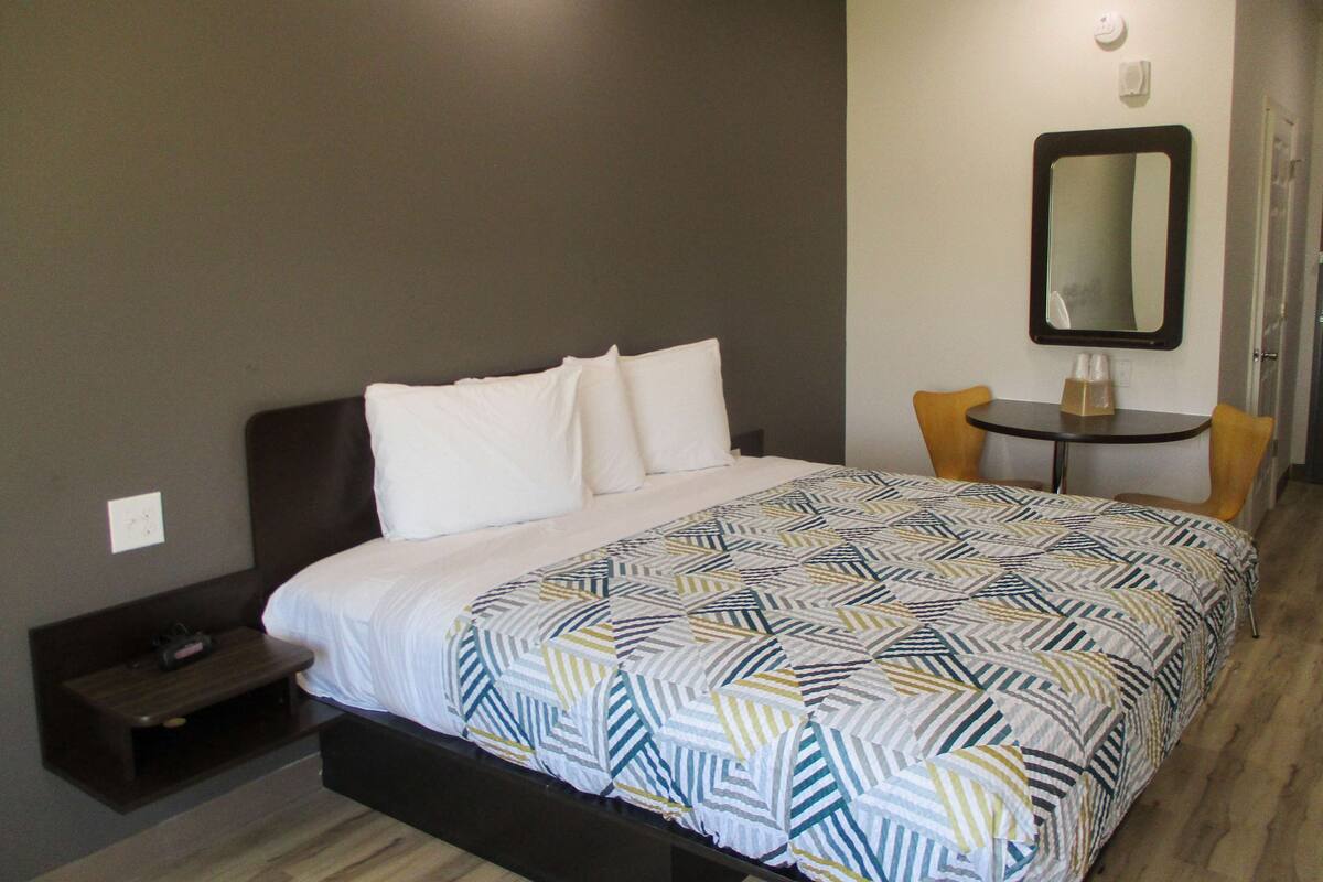 A hotel room with a bed, a small table with two chairs, a mirror, and a nightstand.