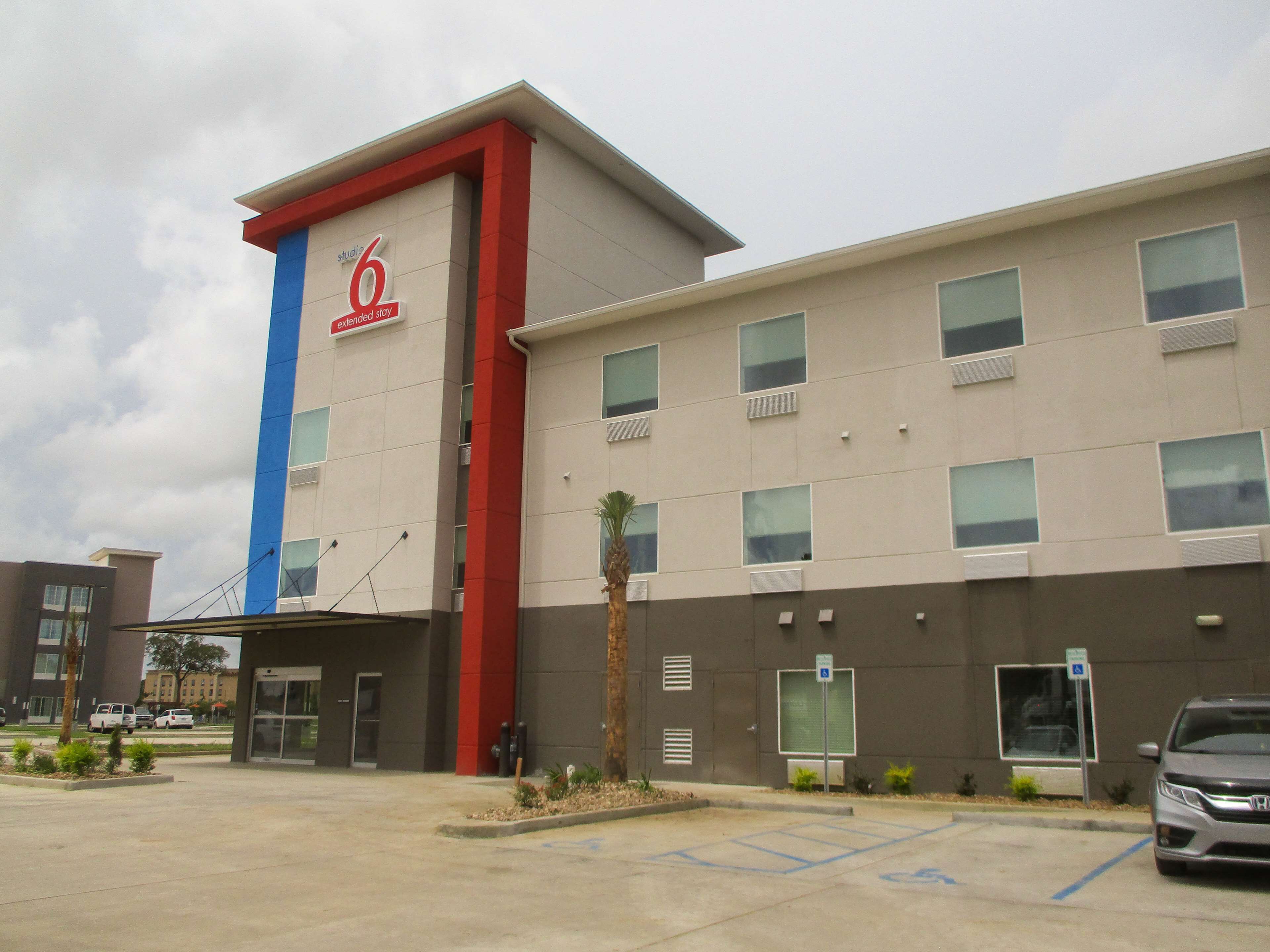 Een hotel met een opvallend rood en blauw logo, meerdere ramen en een parkeerplaats met een parkeerplaats voor mindervaliden.