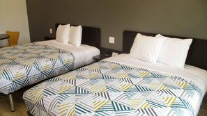 A hotel room with two beds, each with a patterned bedspread and white pillows.
