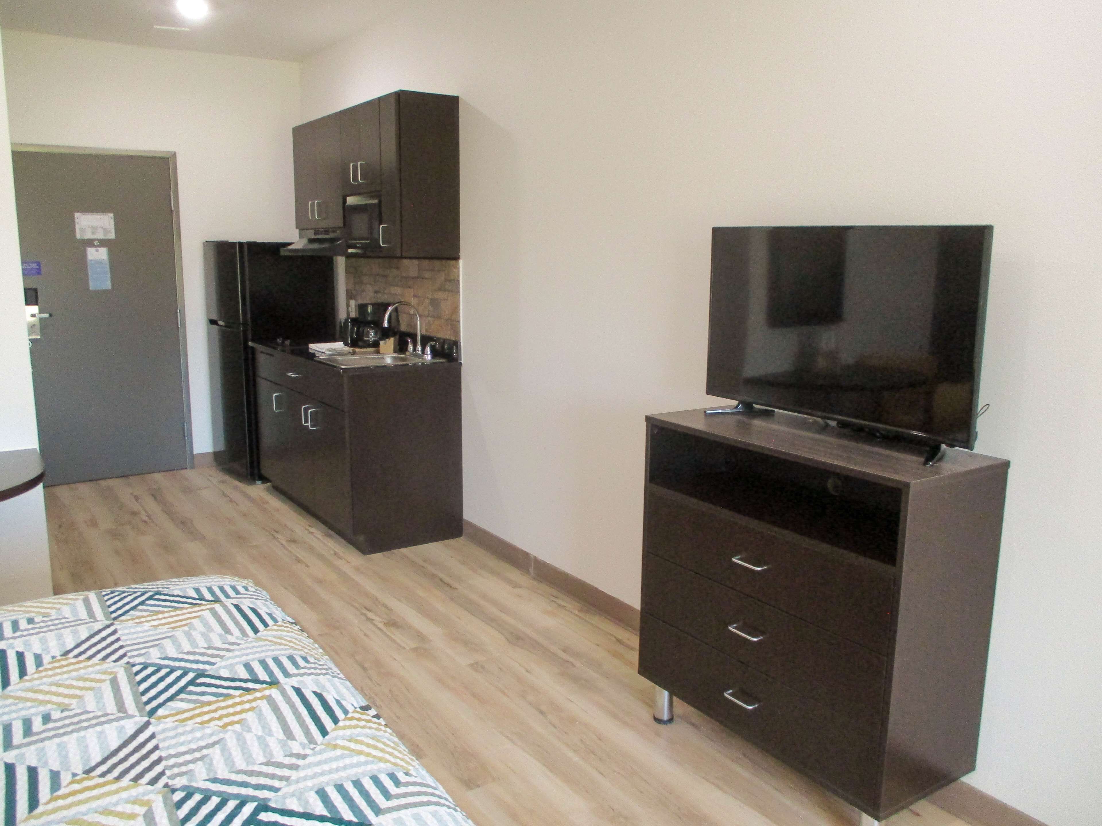 A compact kitchen with dark cabinets, a microwave, and a built-in oven. There's a small sink and a television on a stand.