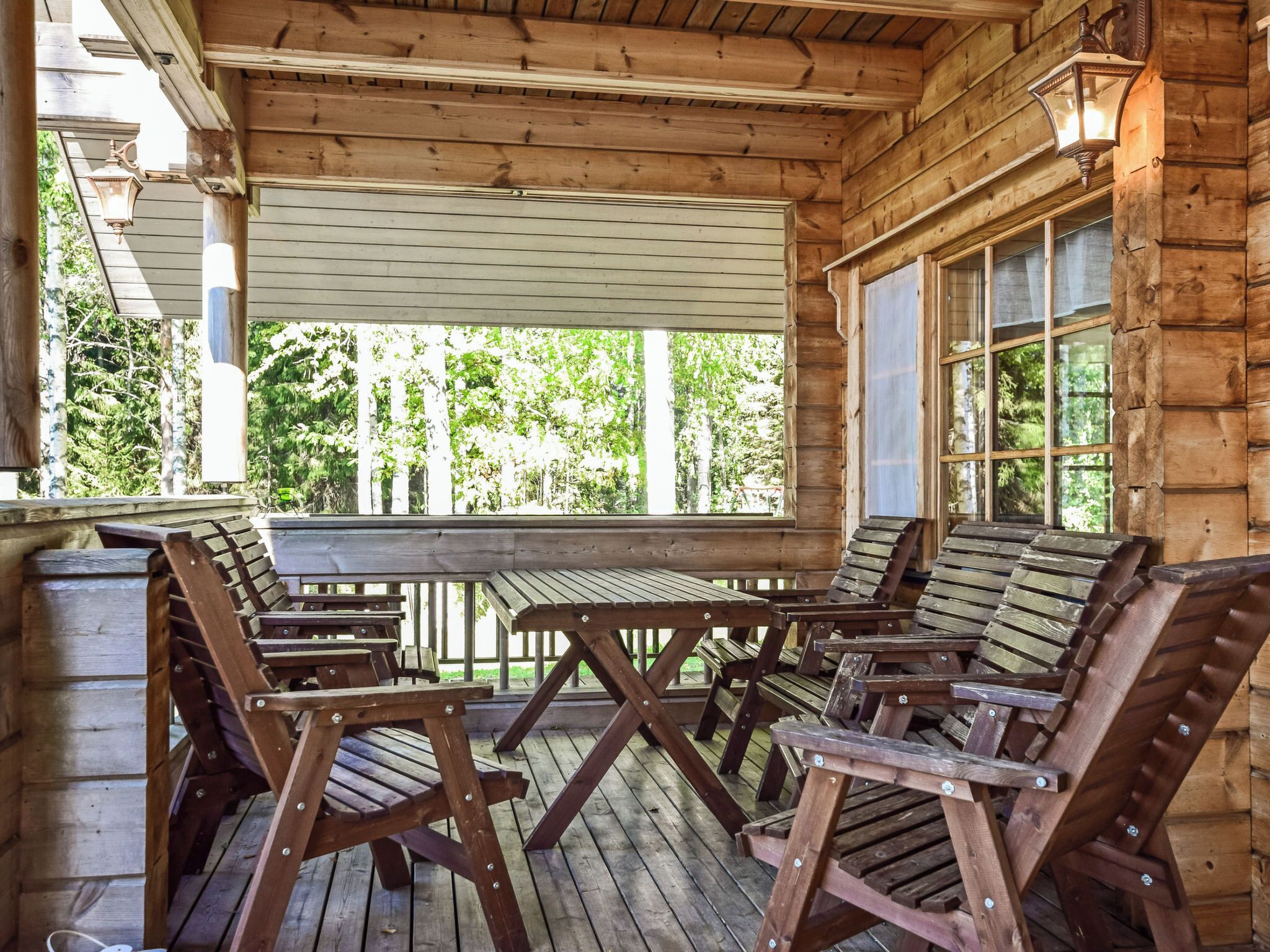 Una terraza de madera con una mesa y sillas, rodeada por una estructura tipo cabaña de madera.