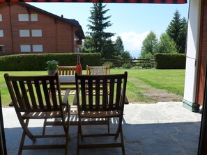 An outdoor patio with a wooden bench and table, a bottle, and a potted plant. - Hyacinthe 2 by Interhome (Villars)