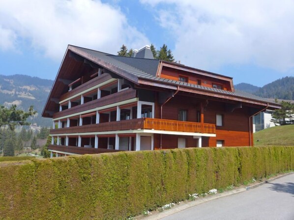 A multi-story wooden building with balconies, set against a mountainous backdrop. - Hyacinthe 2 by Interhome (Villars)