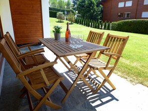 A wooden table and chairs set on a patio with a view of a well-maintained lawn and a building in the background. - Hyacinthe 2 by Interhome (Villars)