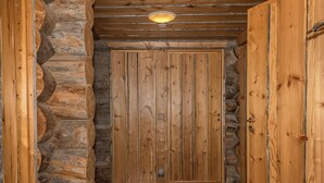 A wooden door with a metal handle and a peephole, flanked by stone walls and a wooden ceiling.