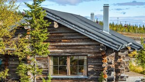 A log cabin with a large window, a chimney, and a wooden deck.