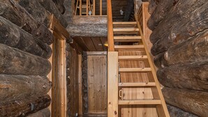 A wooden staircase in a log cabin interior, leading to a loft area.