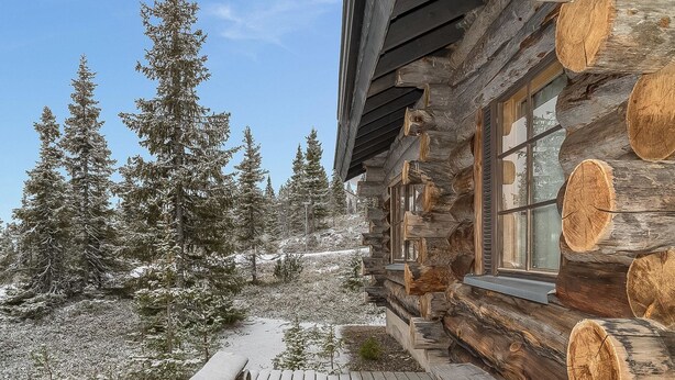 A log cabin with a wooden deck and a snow-covered landscape.