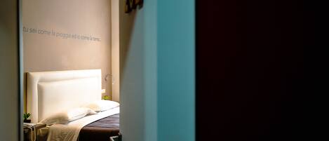 A hotel room with a large bed, a bedside table with a lamp, and a wall with a partial text.