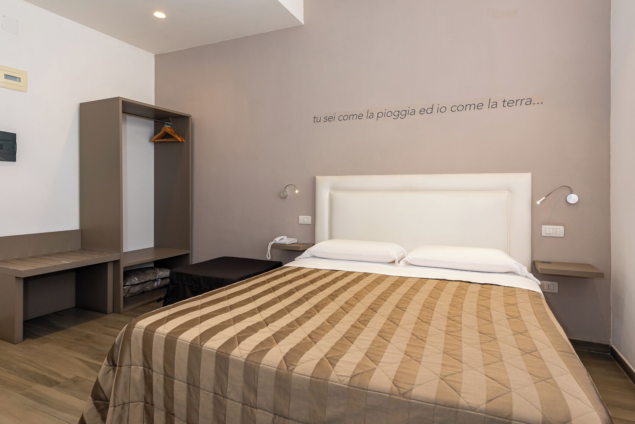 A bedroom with a bed, bedside tables, a wardrobe, and a wall with a quote.