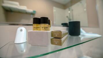 A bathroom counter with a glass top, a white soap dispenser, three bottles of argan oil, and two cardboard boxes.