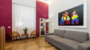 Ein Wohnzimmer mit grauem Sofa, zwei Holzstühlen, einem Blumentopf und einem gerahmten abstrakten Gemälde an der Wand.