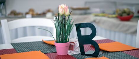 Una mesa con una maceta rosa, una letra 'B' negra y manteles individuales naranja.